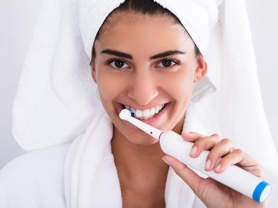 Beautiful smiling young woman using electric toothbrush