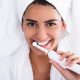 Beautiful smiling young woman using electric toothbrush